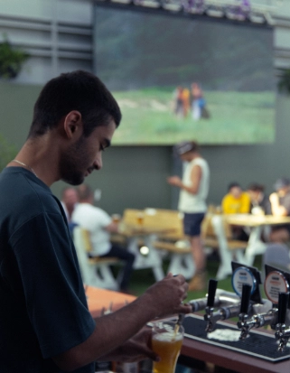 A bartender serving drinks at a large beergarden with sports playing in the background