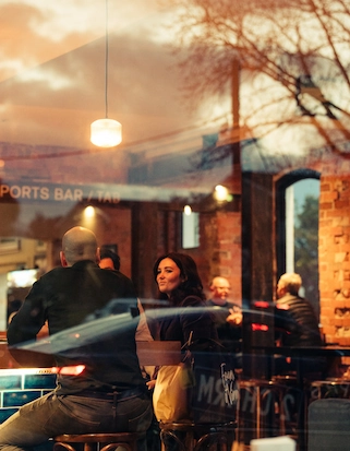 A view from outside looking in through a window and seeing people dining at different tables in a historic pub