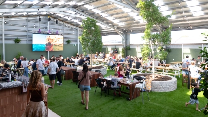 A large covered beer garden with trees, grass, TVs, and a bar
