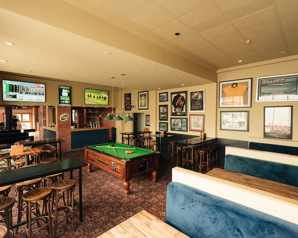 An overview of the Queen of the West Sports Bar showing booths, a pool table, tall tables and chairs, sports memorabilia and a bar.